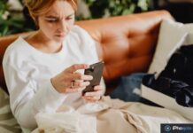 Apple met en garde contre des arnaques qui passent par FaceTime Femme inquiète utilisant un smartphone sur un canapé