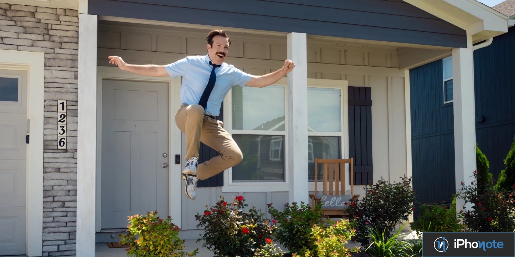 Ted Lasso saute joyeusement devant une maison résidentielle